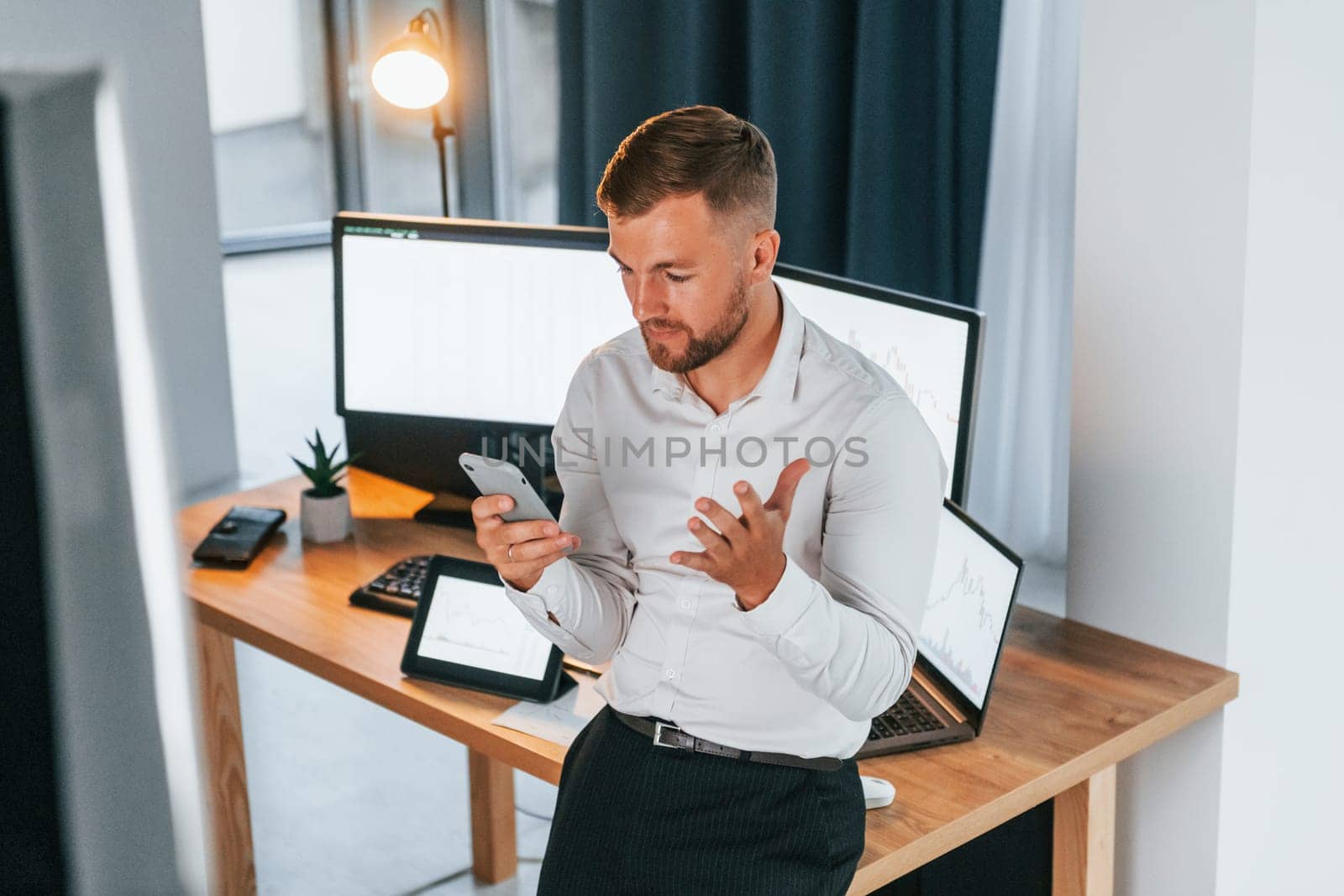 Busy day. Young businessman in formal clothes is in office with multiple screens.