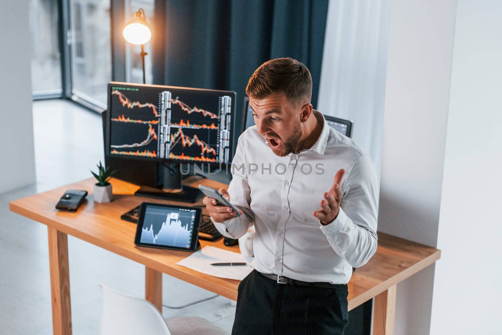 Near the table. Young businessman in formal clothes is in office with multiple screens.