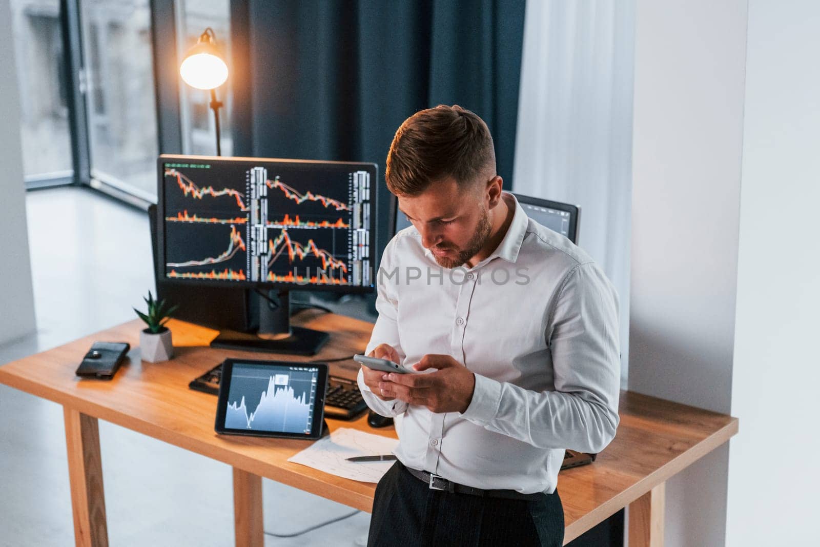 Near the table. Young businessman in formal clothes is in office with multiple screens.