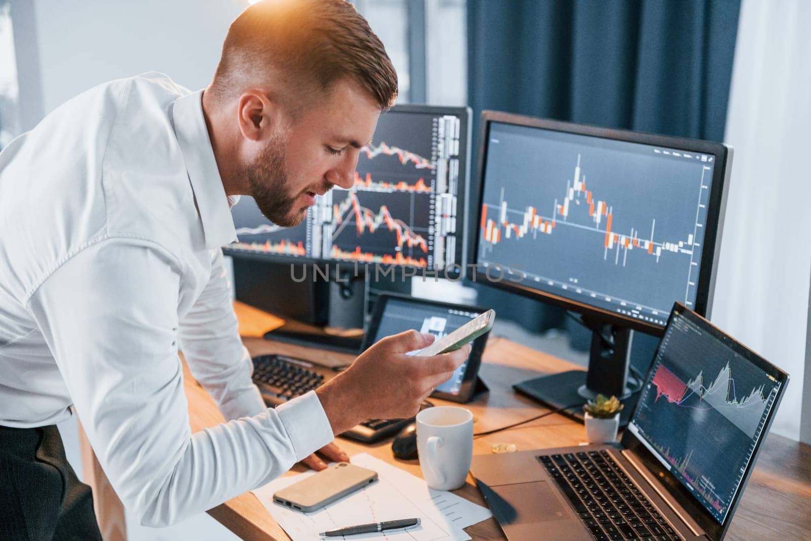 Near the table. Young businessman in formal clothes is in office with multiple screens.