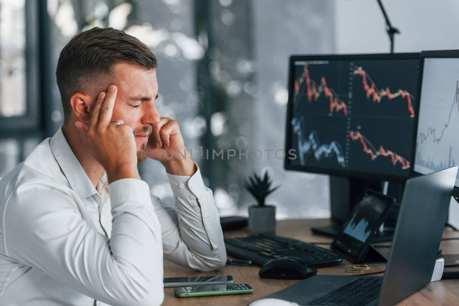 Young businessman in formal clothes is in office with multiple screens.