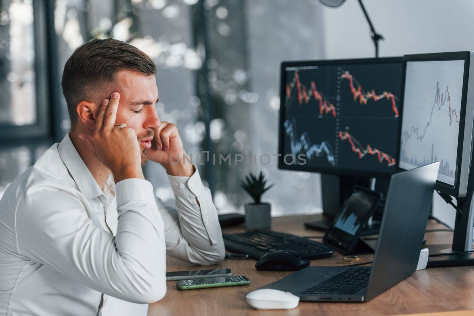 Young businessman in formal clothes is in office with multiple screens.