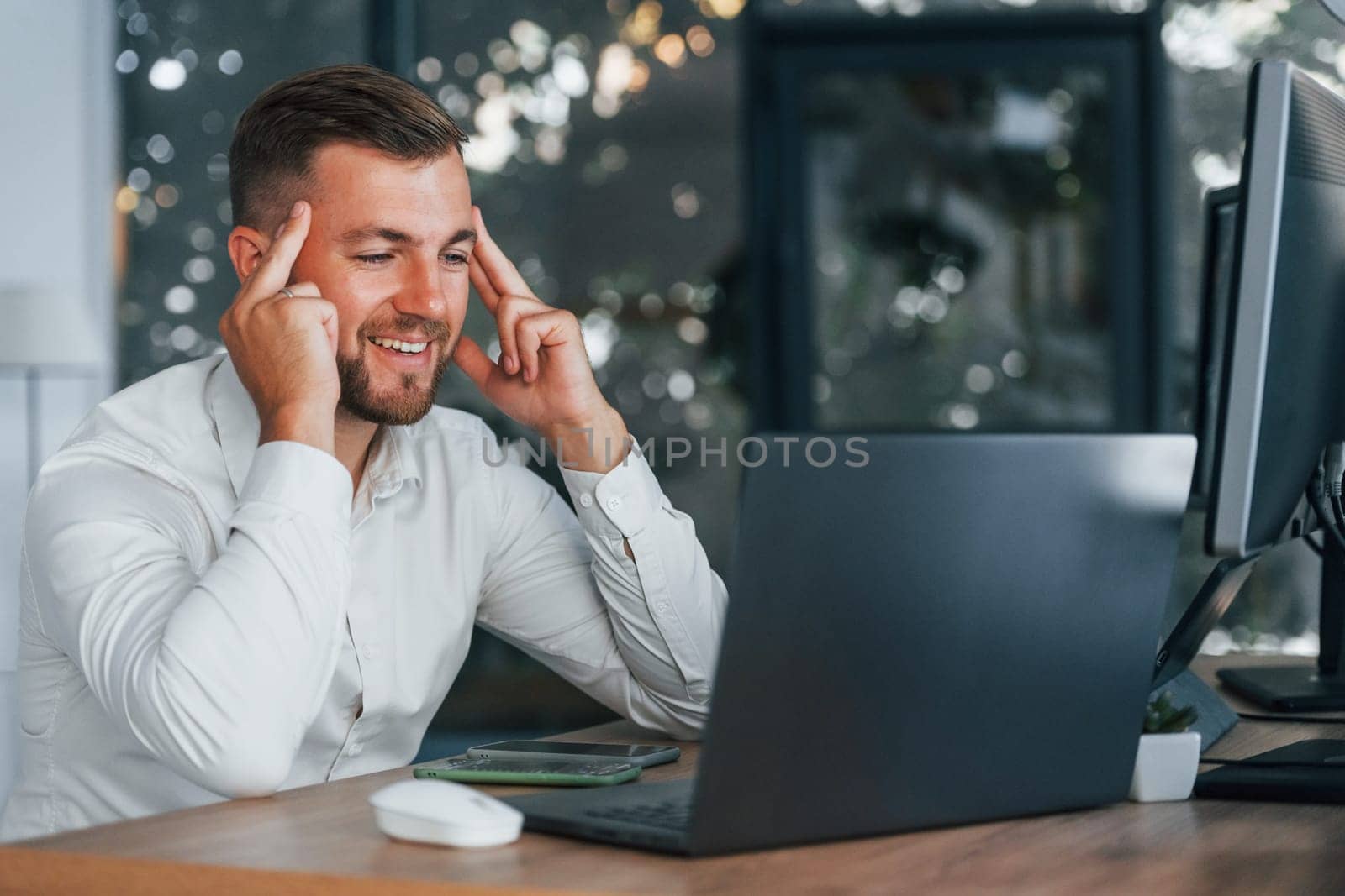Young businessman in formal clothes is in office with multiple screens.