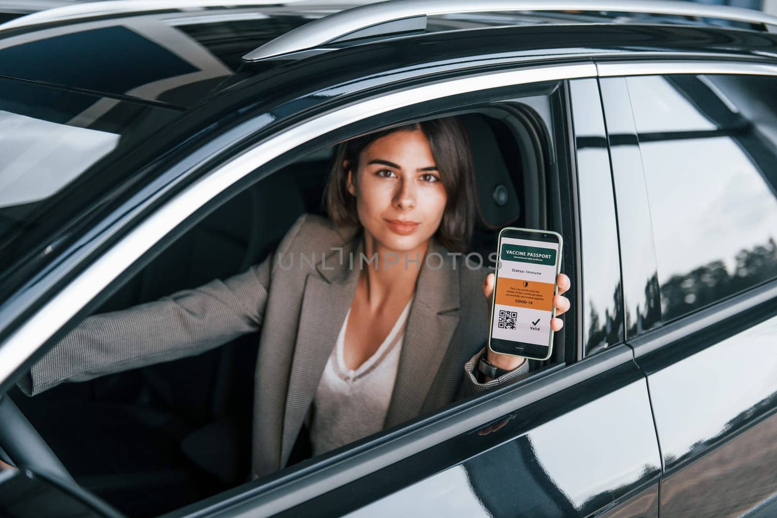 Holding smartphone with digital vaccine passport. Woman testing new car. Sitting indoors in modern automobile.
