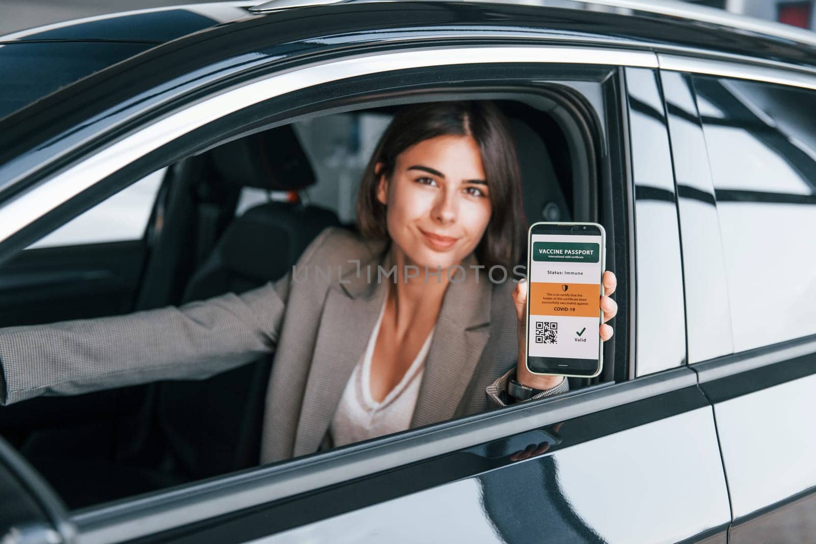 Holding smartphone with digital vaccine passport. Woman testing new car. Sitting indoors in modern automobile.