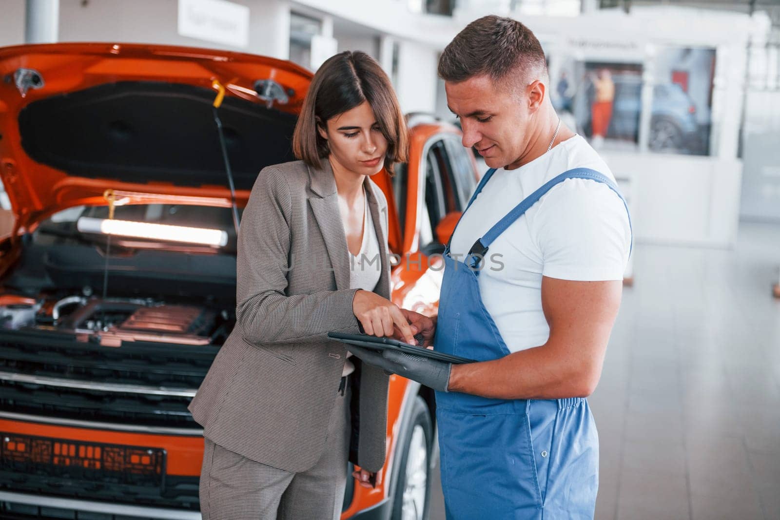Two people. Man repairing woman's automobile indoors. Professional service.