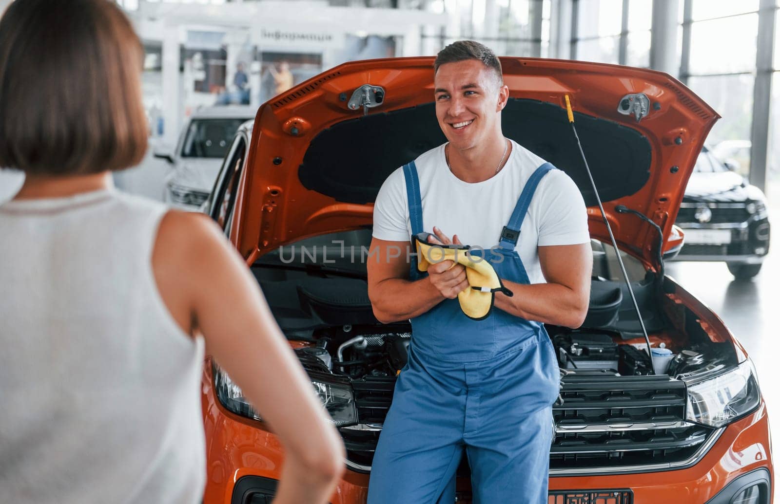 Owner standing near the man that repairing automobile indoors. Professional service.