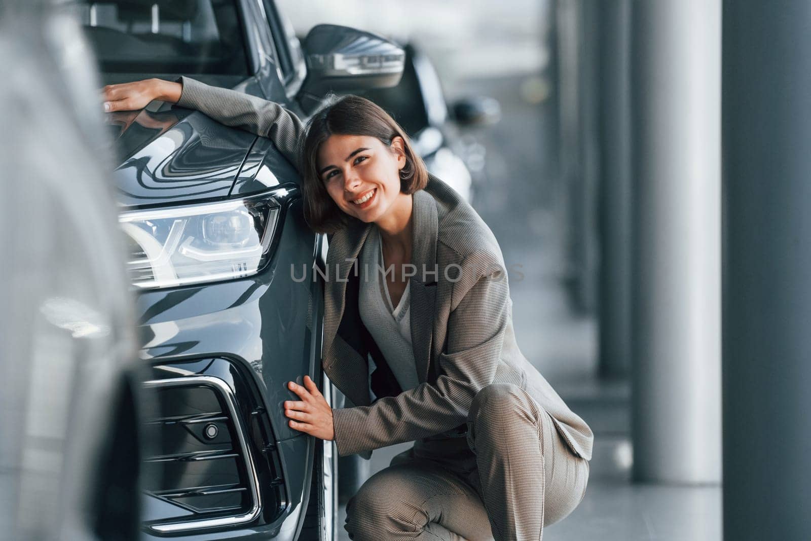 Embracing the car. Woman is indoors near brand new automobile indoors.