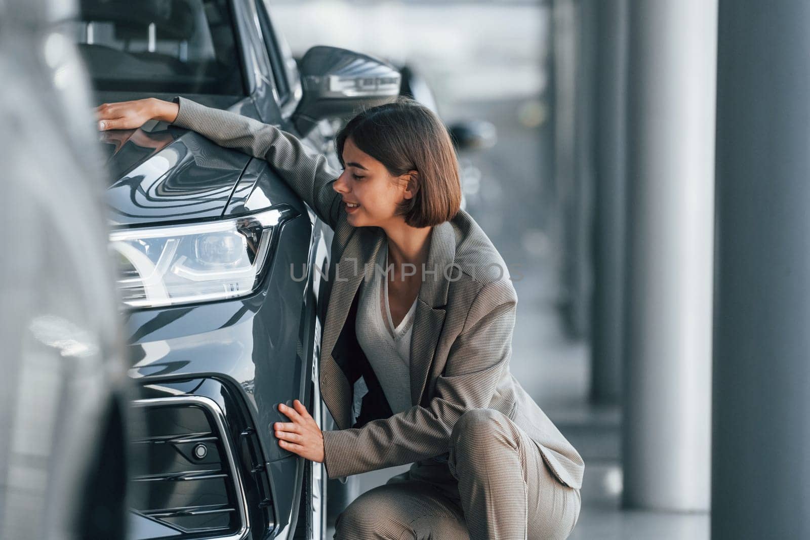 Embracing the car. Woman is indoors near brand new automobile indoors.