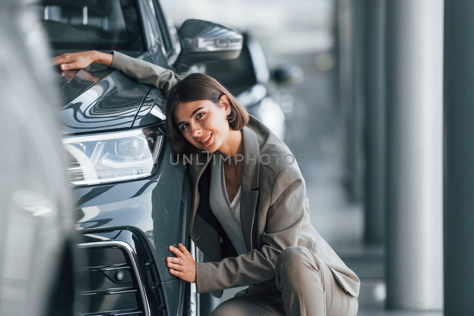 Embracing the car. Woman is indoors near brand new automobile indoors.