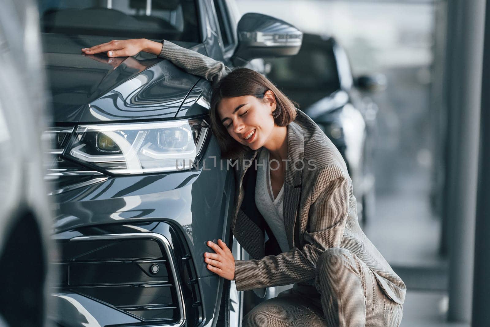 Embracing the car. Woman is indoors near brand new automobile indoors.