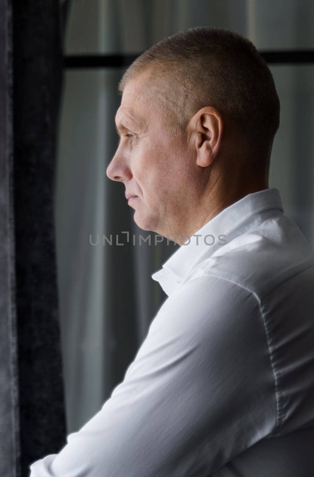 Portrait of a pensive male businessman who stands and looks out the window. Vertical frame.