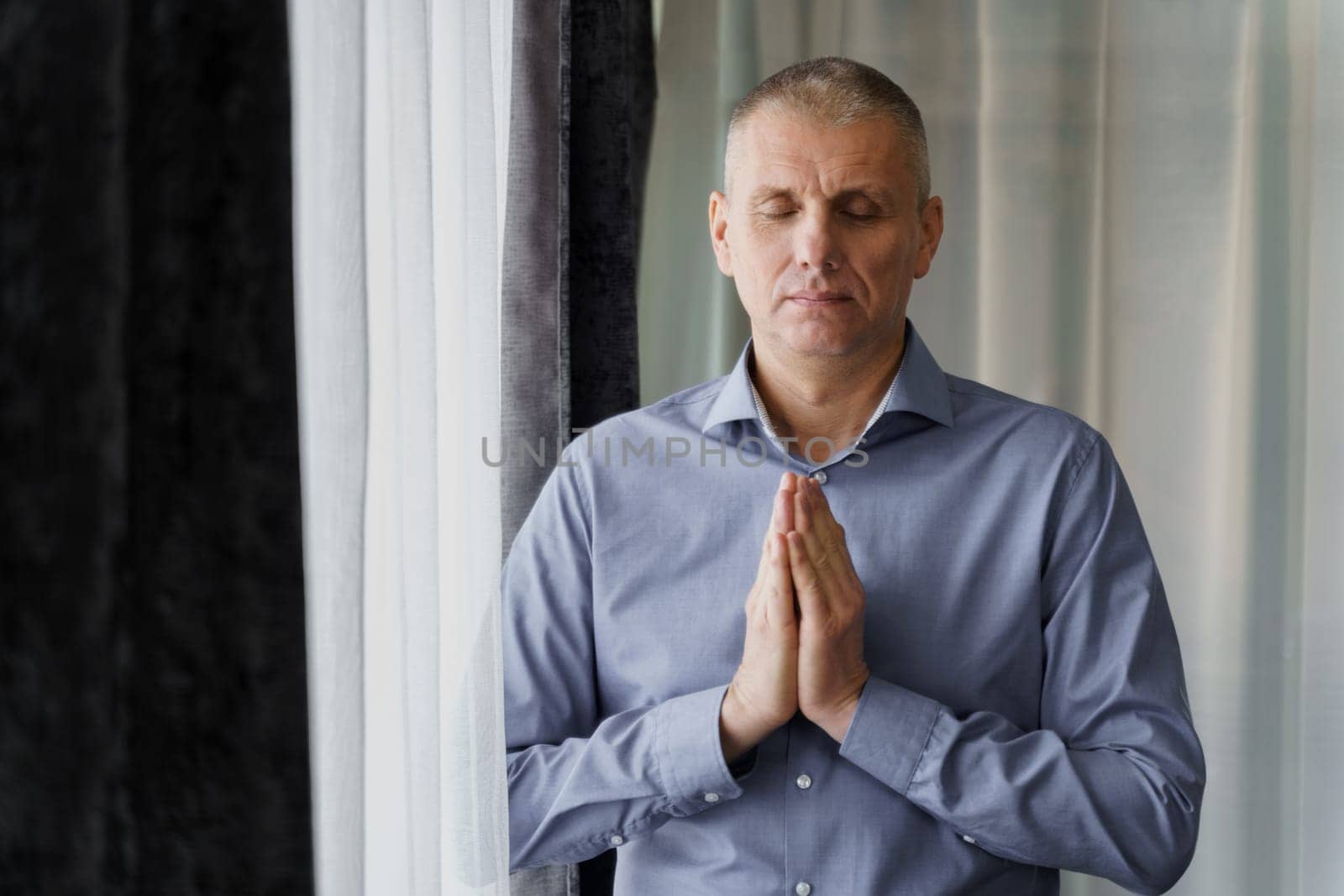 A man - a businessman stands near the window does relaxing breathing exercises - meditates. A break during work.