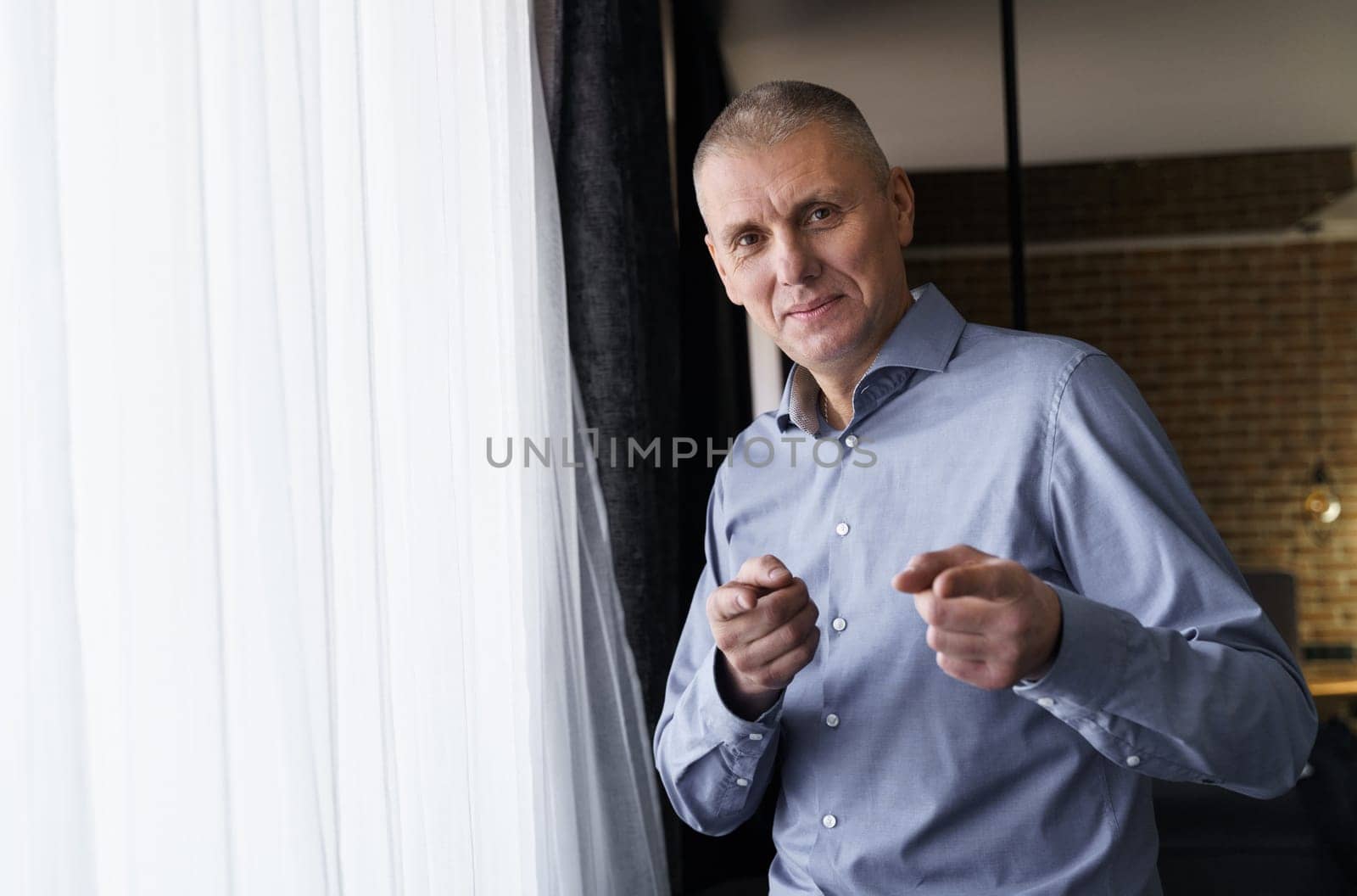 Confident smiling businessman in a blue shirt pointing with index fingers at the camera. The concept of people and gestures.