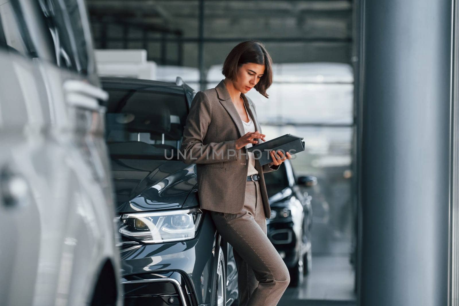 With tablet in hands. Woman is indoors near brand new automobile indoors.
