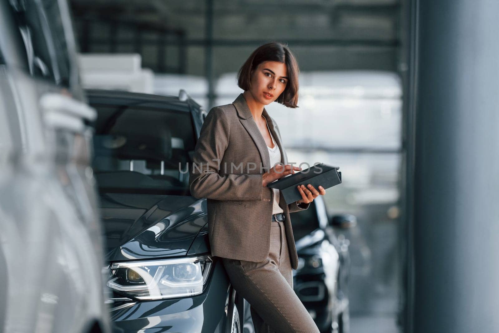 With tablet in hands. Woman is indoors near brand new automobile indoors.