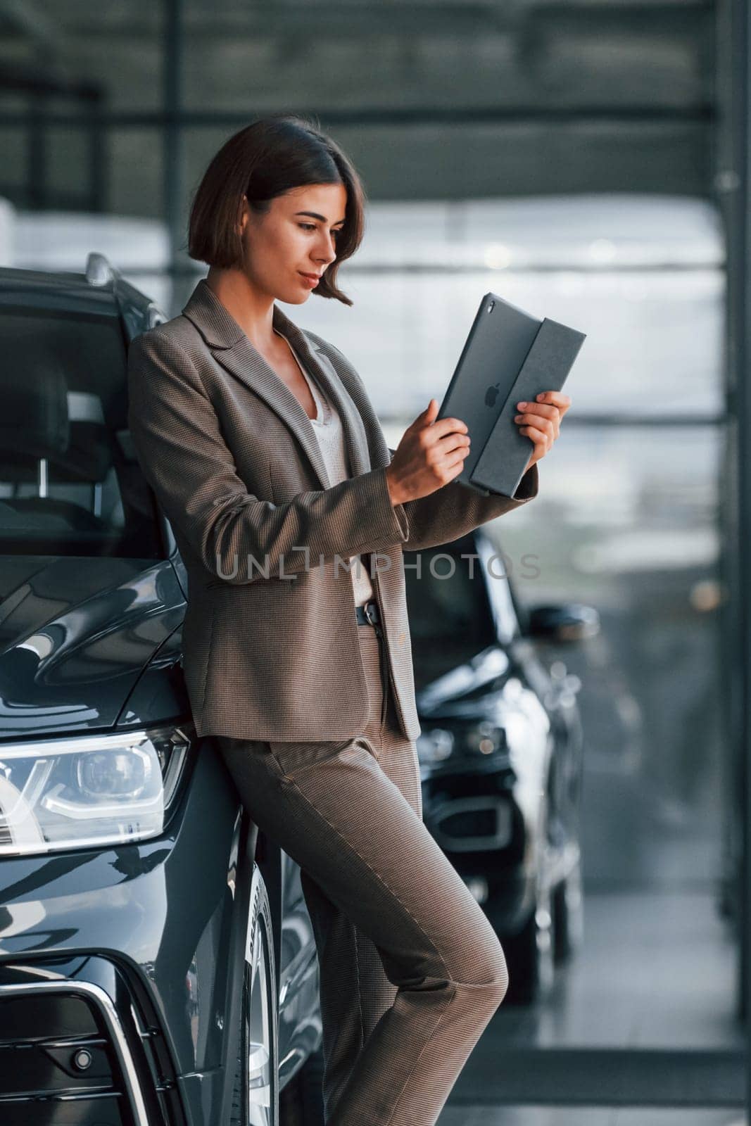 With tablet in hands. Woman is indoors near brand new automobile indoors.