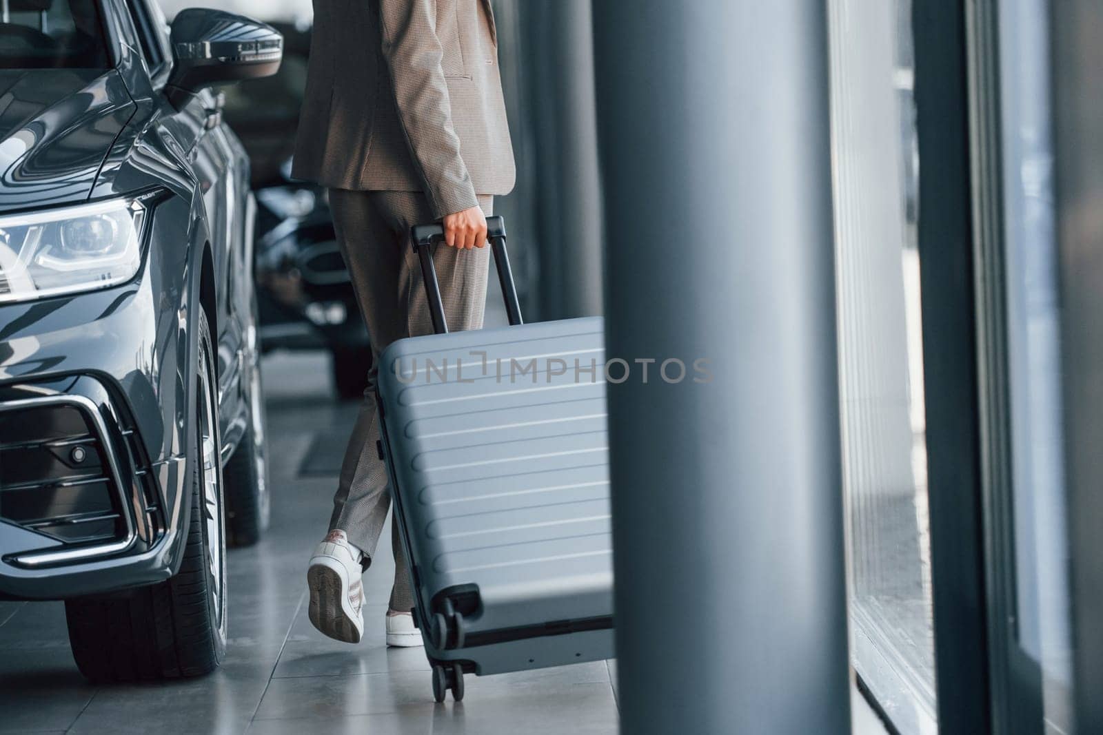 Holding luggage. Woman is indoors near brand new automobile indoors.