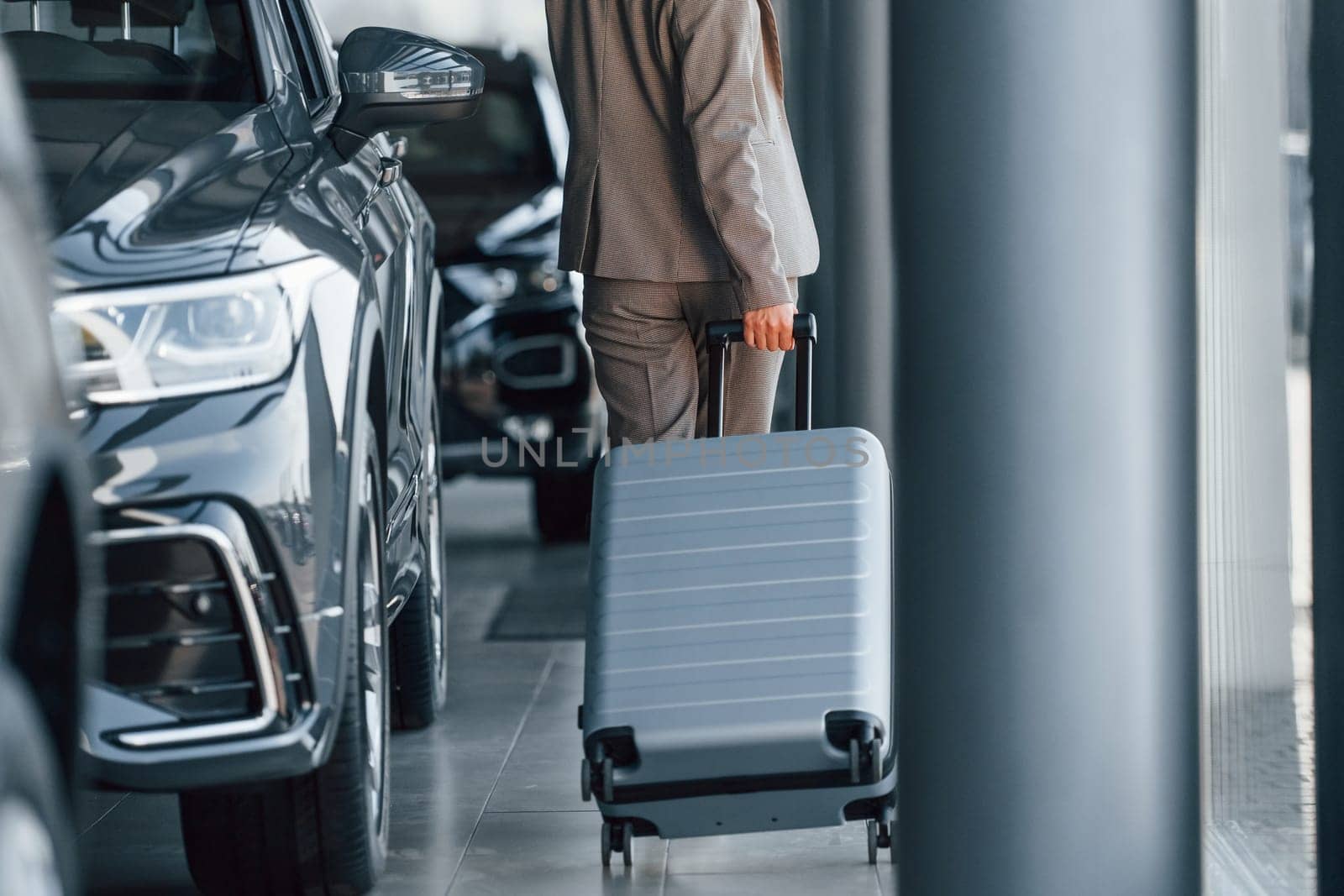 Holding luggage. Woman is indoors near brand new automobile indoors.