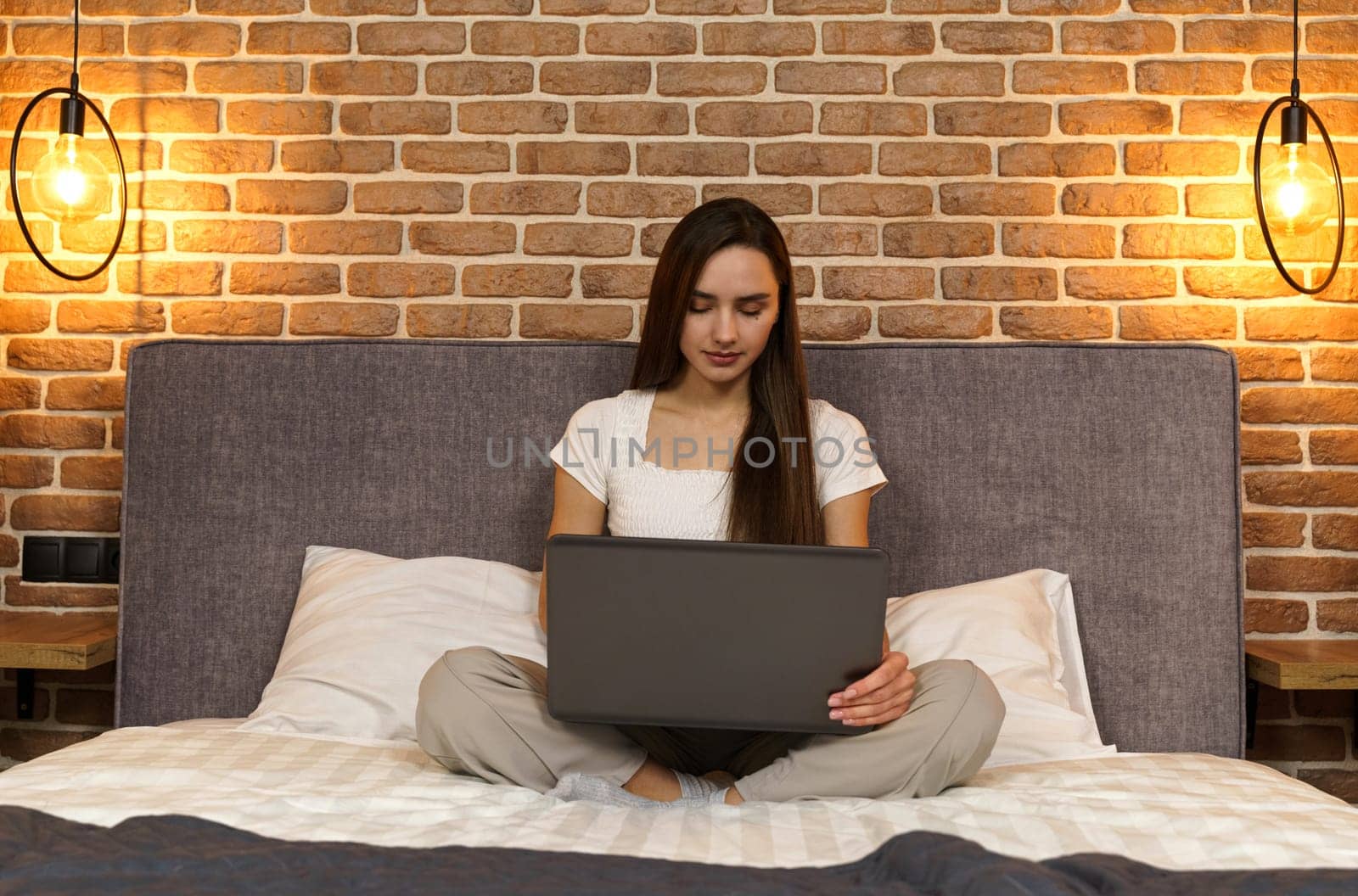 Happy beautiful woman is sitting on the bed and working on the laptop.