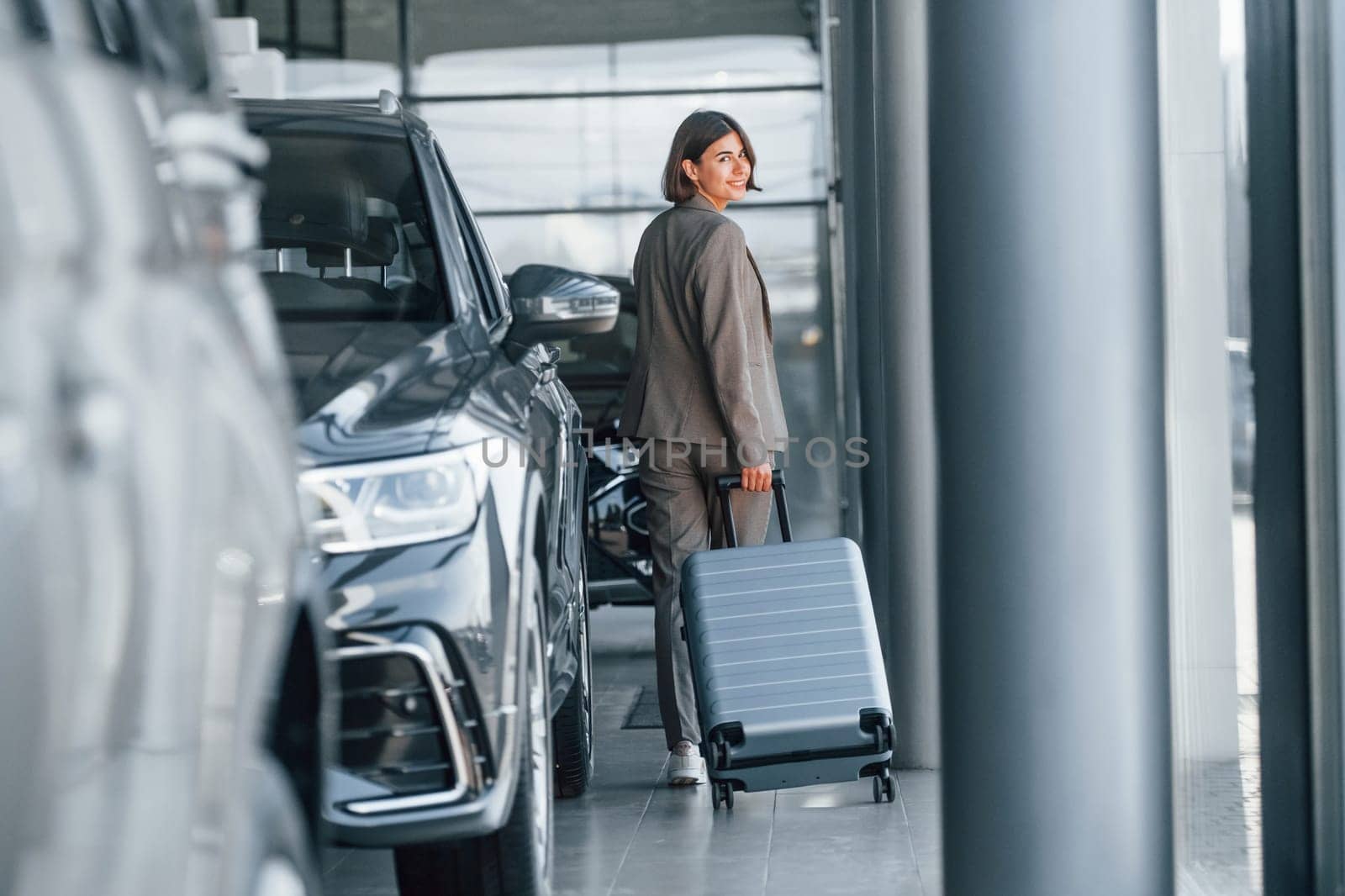 Holding luggage. Woman is indoors near brand new automobile indoors.