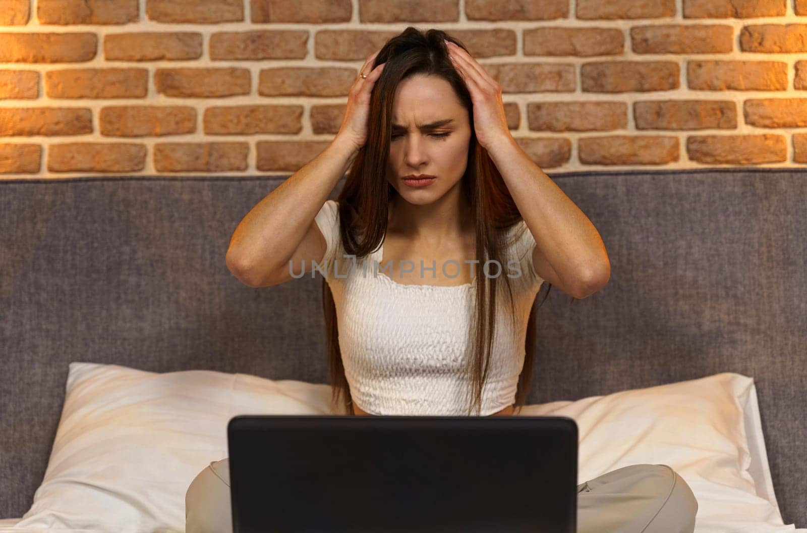 Young business woman with a headache, uses a laptop, works late at night on the bed by Sd28DimoN_1976