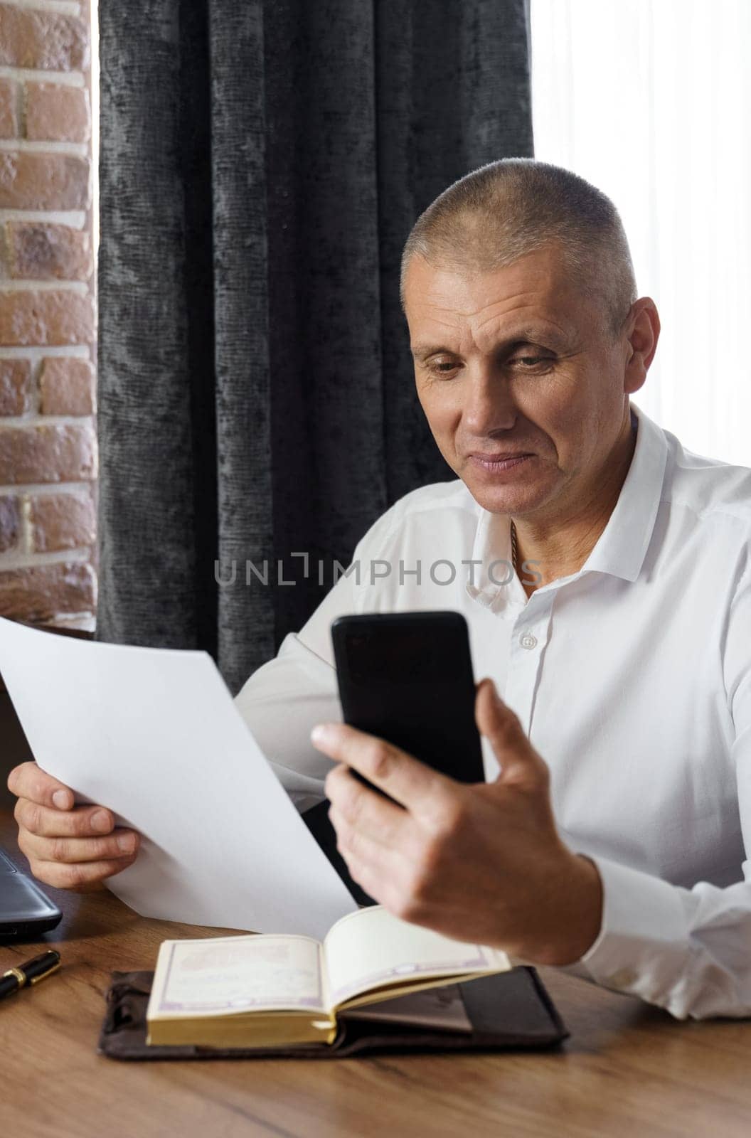 A businessman holds a phone and documents in his hands, reads information from the phone. Financial manager, company.