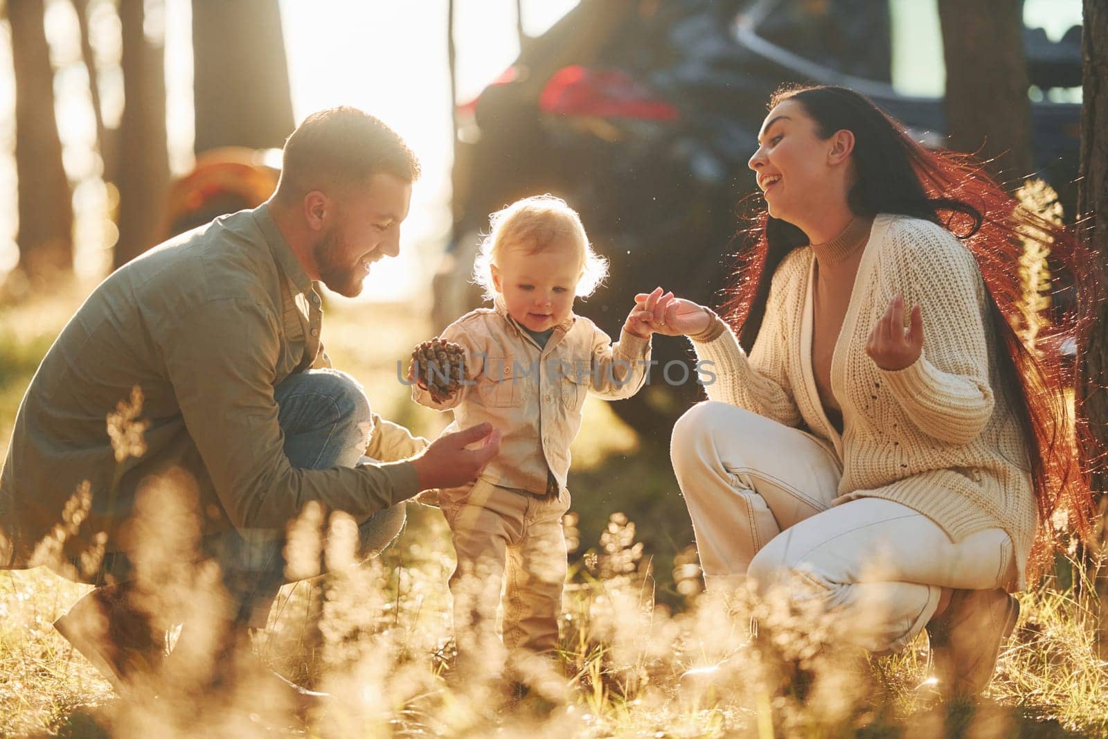 Sitting on the ground. Happy family of father, mother and little daughter is in the forest.