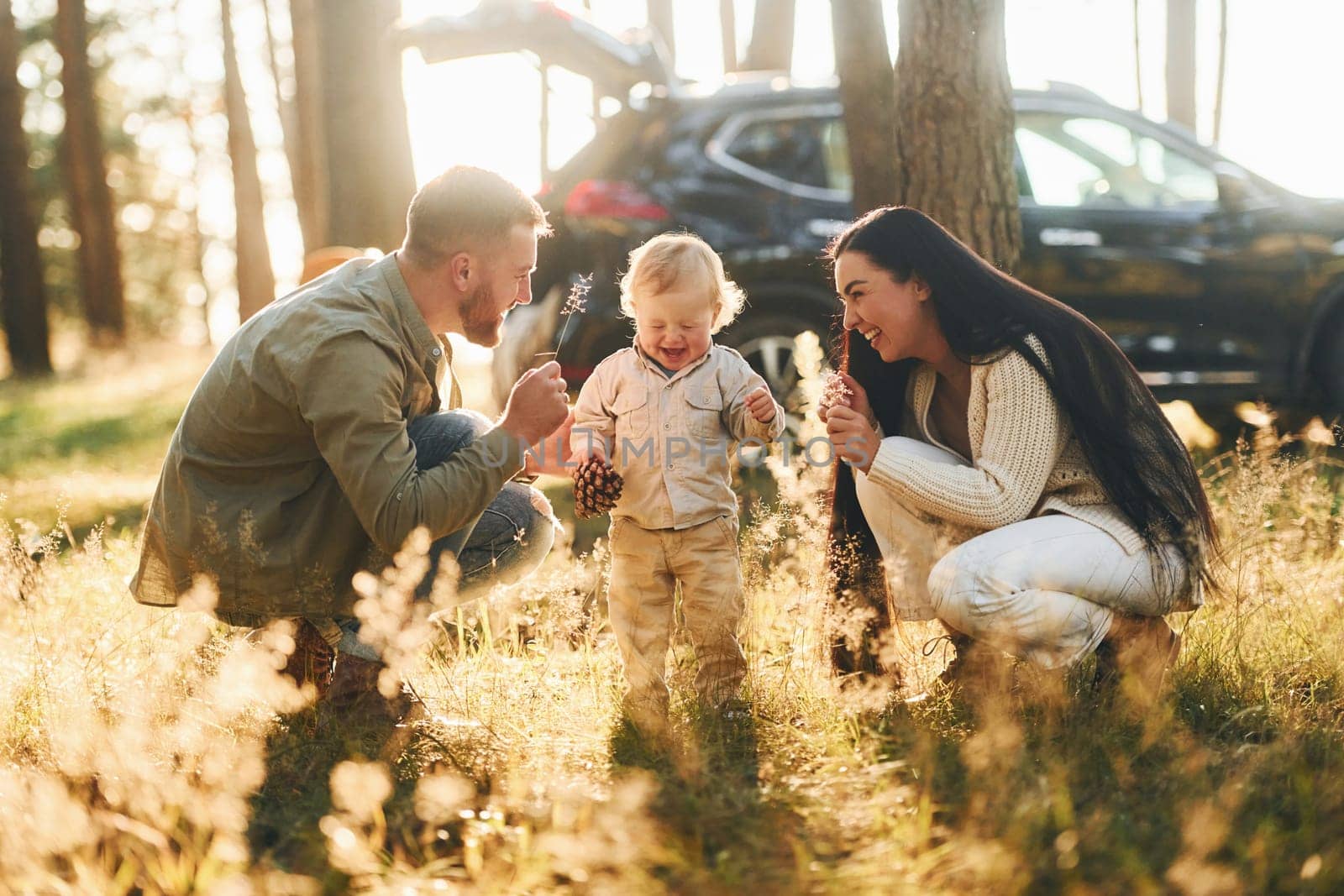 Sitting on the ground. Happy family of father, mother and little daughter is in the forest by Standret