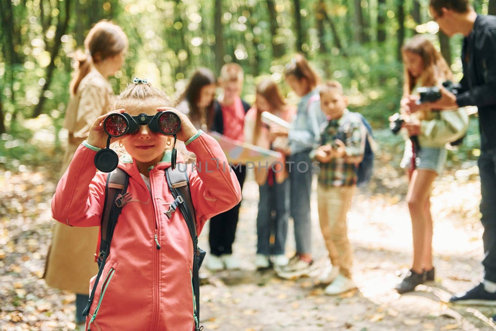 Girl looking into binoculars. Kids in green forest at summer daytime together.