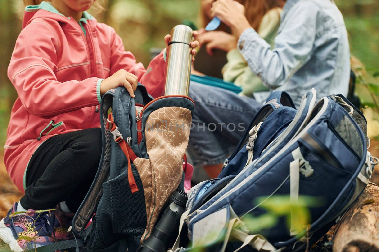 Two people sitting and resting. Kids in green forest at summer daytime together.