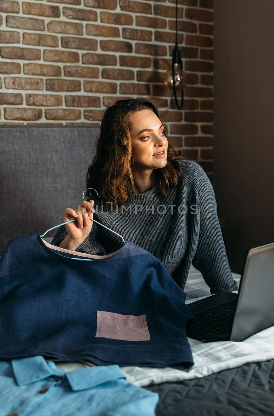 A young woman sits on a bed and admires her purchases made through an online store.