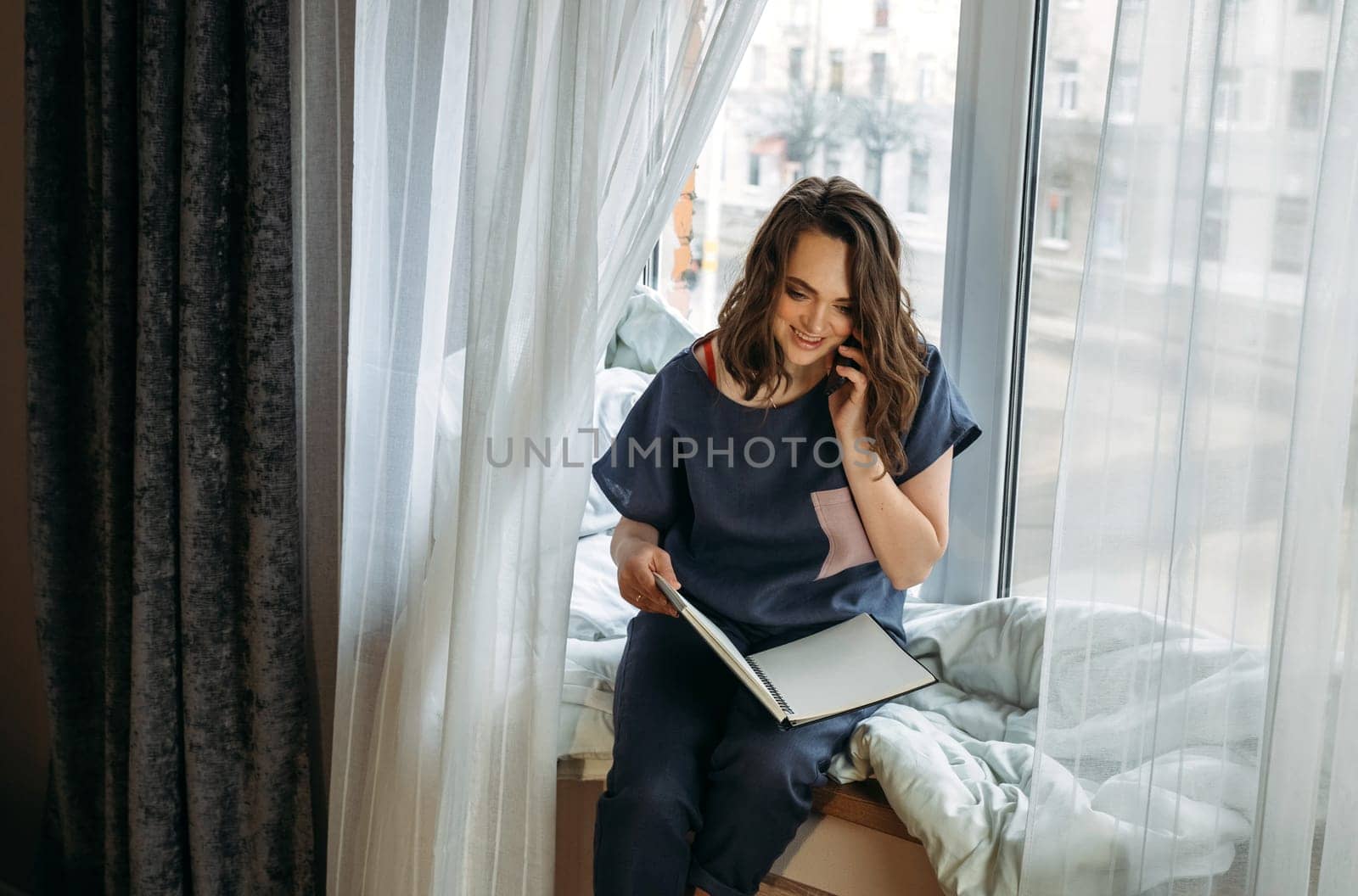A young woman sitting on a windowsill talking to clients, holding a notepad in her hands by Sd28DimoN_1976