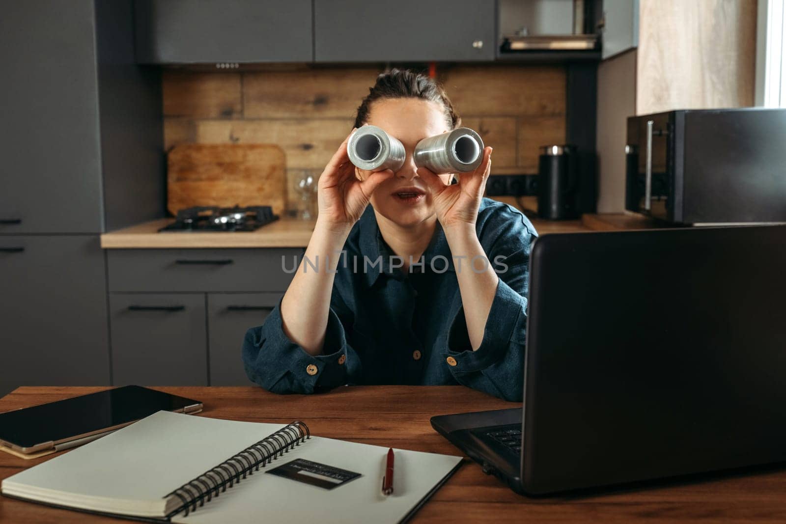 Portrait of a beautiful cheerful female clothing stylist who sits at a table near a laptop and looks through large spools of thread.