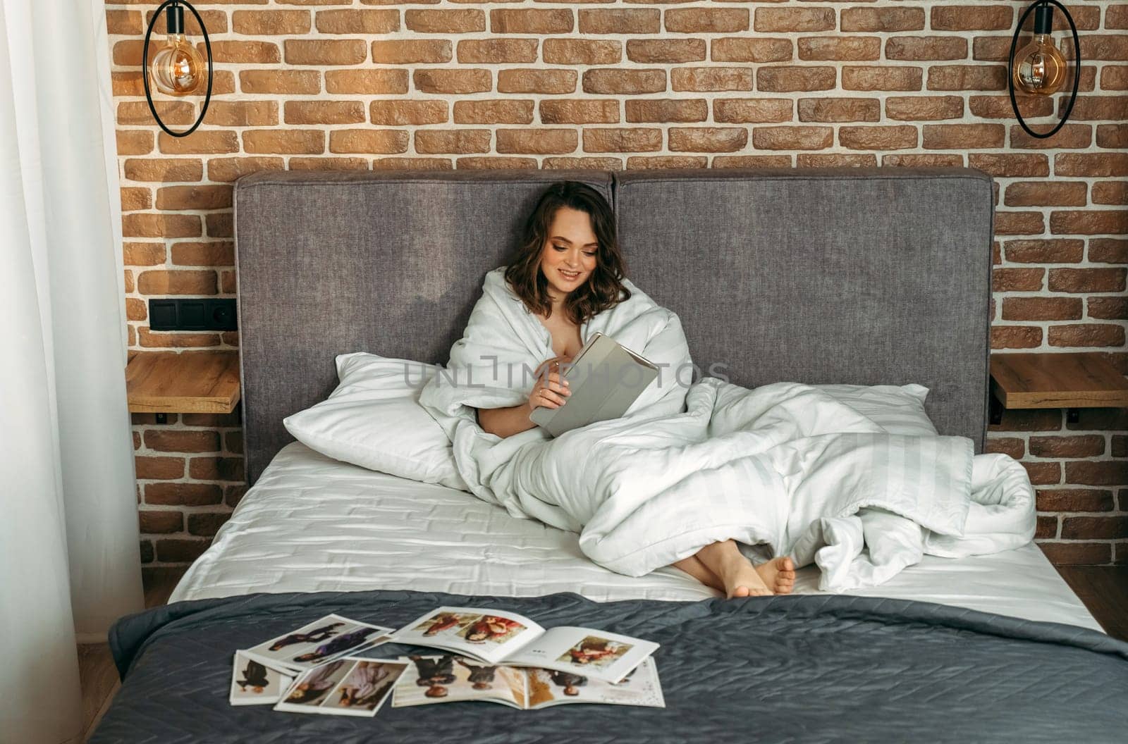 A young woman lies in bed, makes online purchases through a tablet, catalogs with clothes lie in front of her. by Sd28DimoN_1976