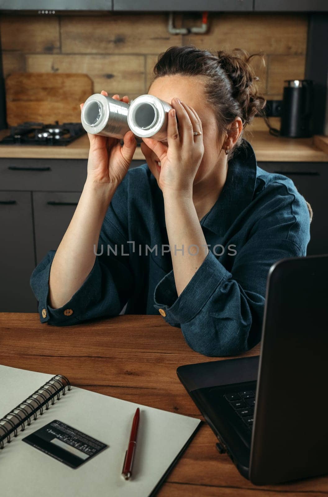 Portrait of a beautiful cheerful female clothing stylist who sits at a table near a laptop and looks through large spools of thread. Vertical frame.