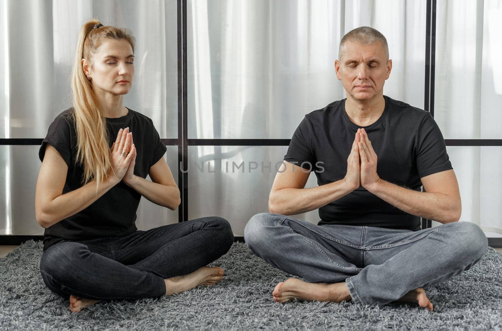 Man and woman practice yoga and meditate for relaxation and balance of life on a mat in a room at home. Sports concept.