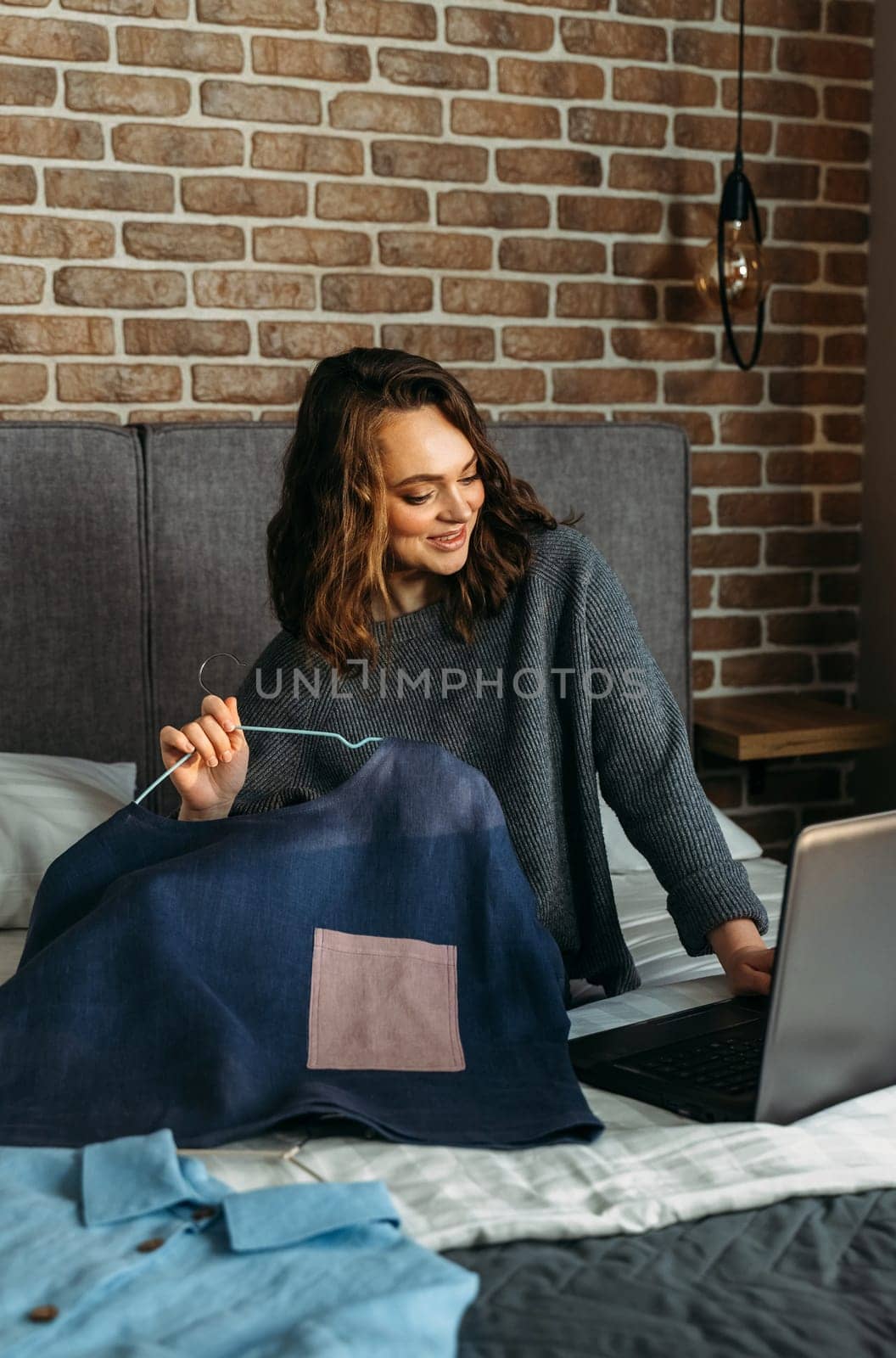 A young woman sits on a bed and admires her purchases made through an online store. Writes a review about the purchase of goods on a laptop.