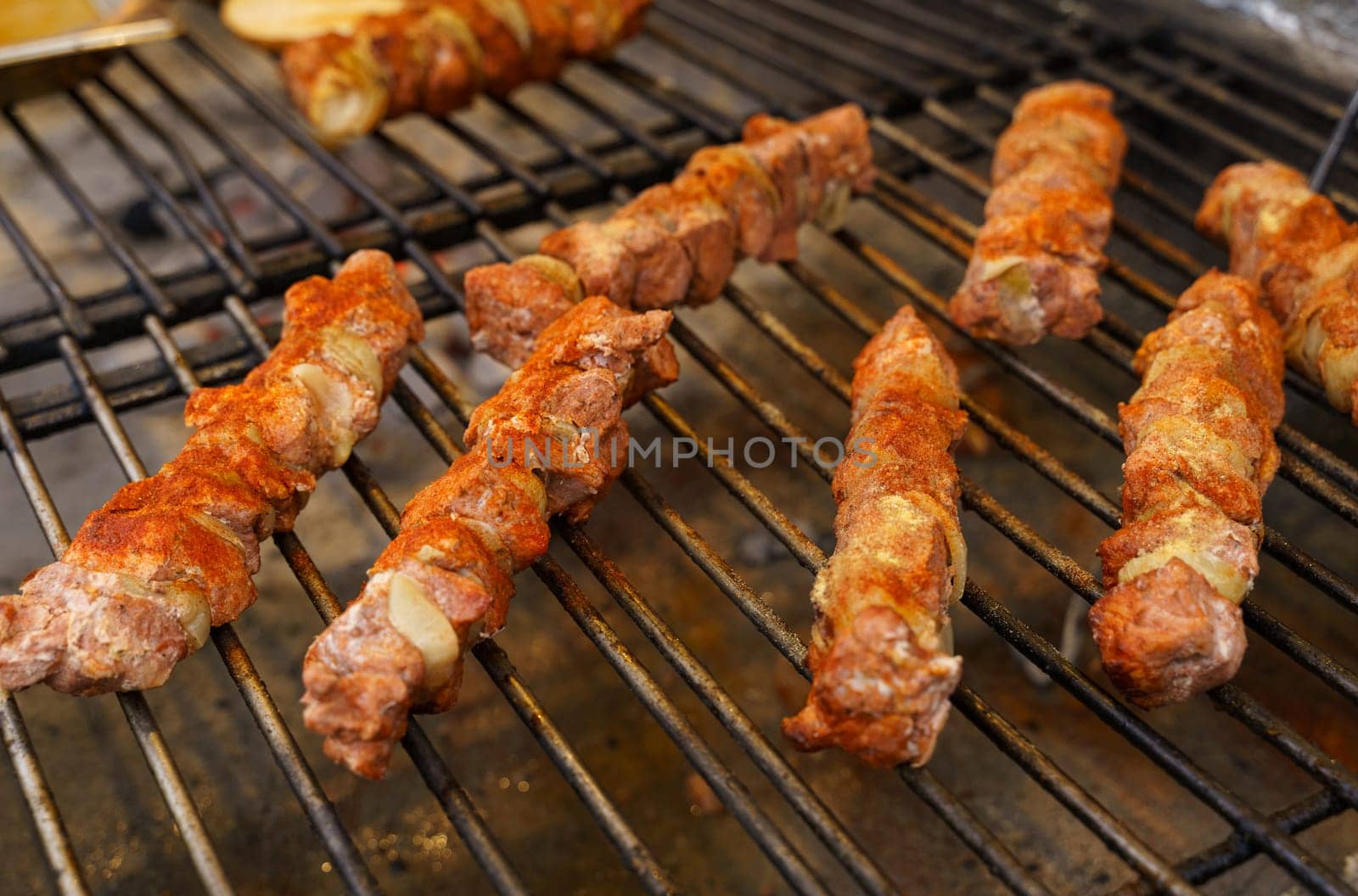 Fried meat with onions on a skewer lies on the grate. Polish street food.
