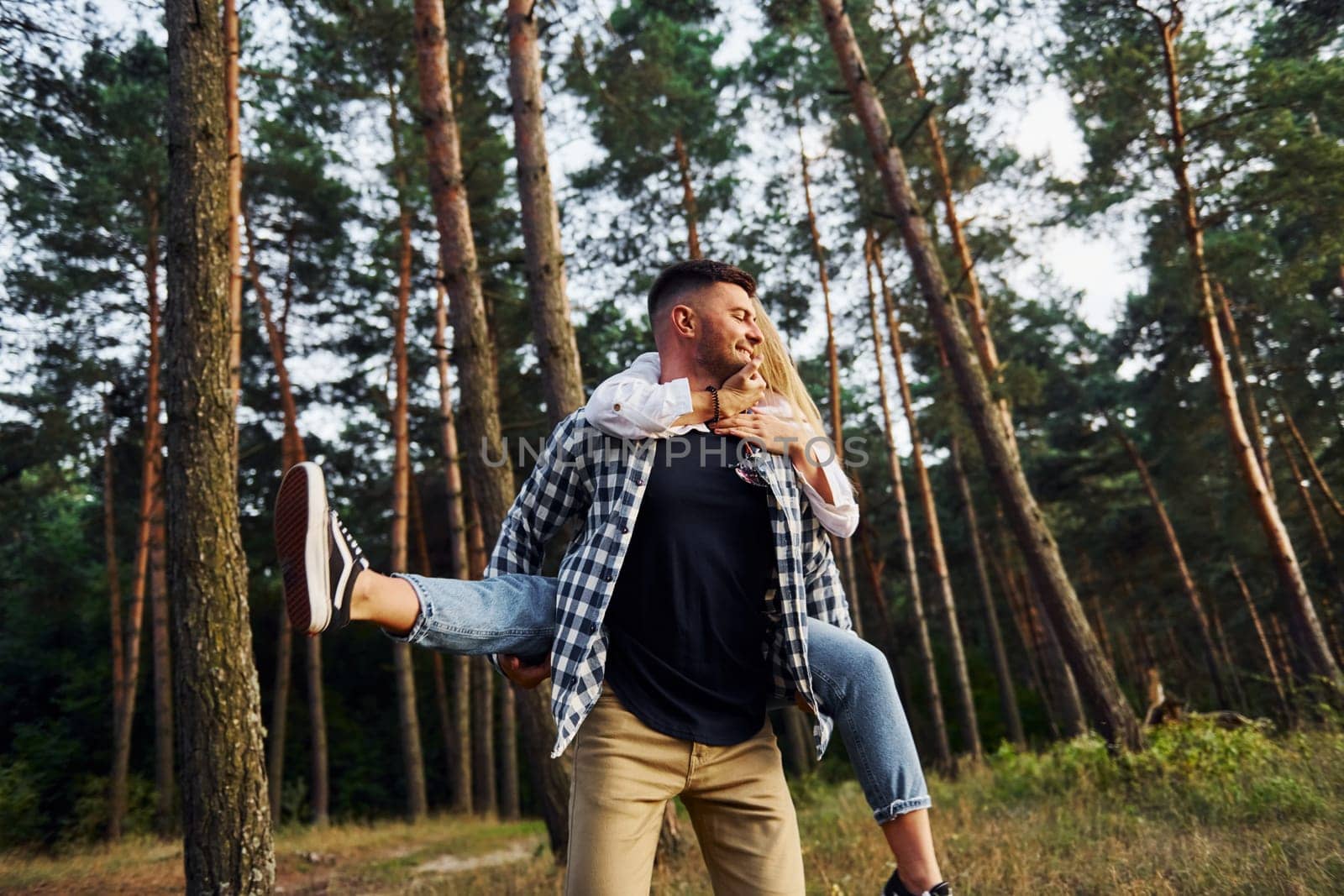 Woman is riding her man. Happy couple is outdoors in the forest at daytime.