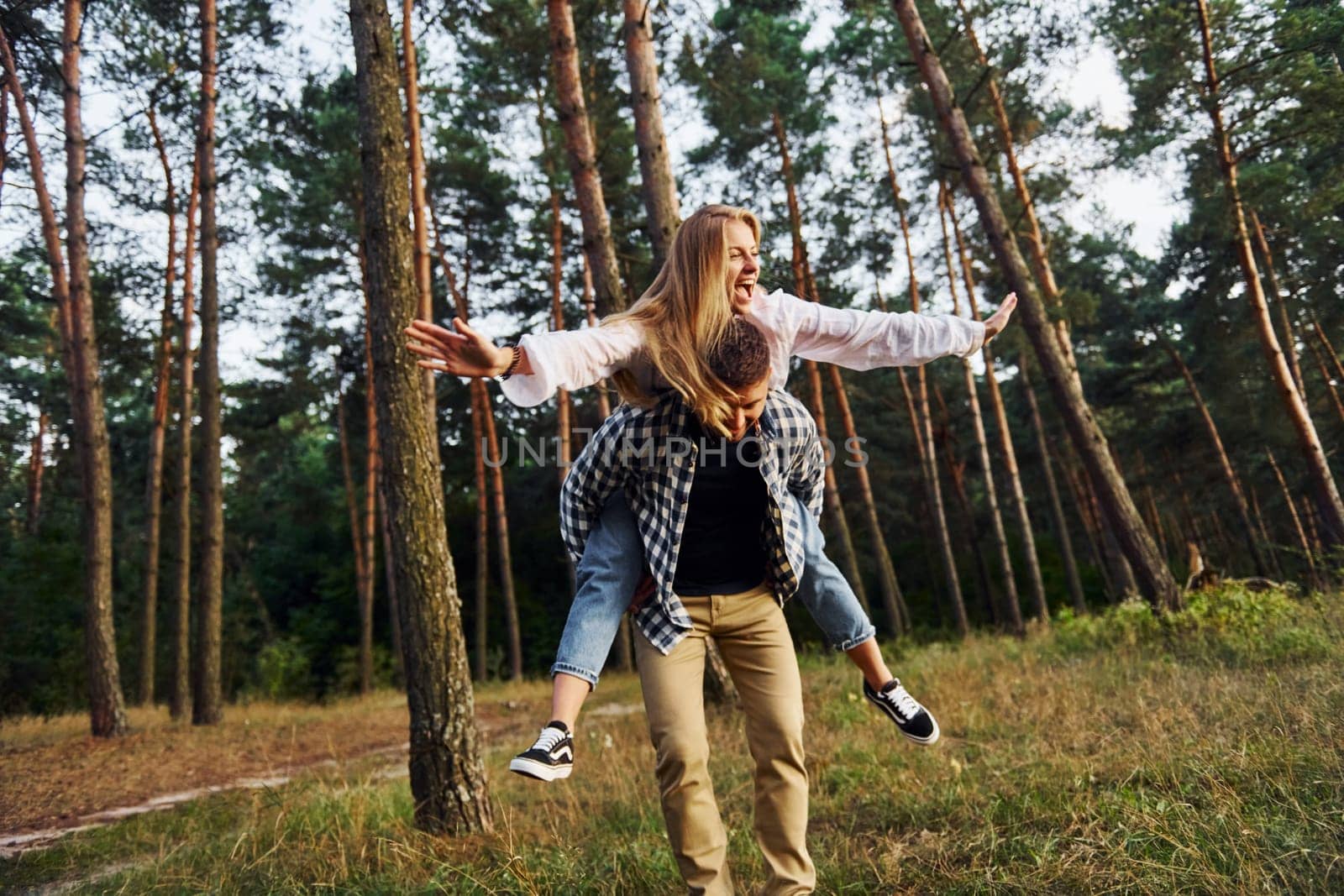 Woman is riding her man. Happy couple is outdoors in the forest at daytime.