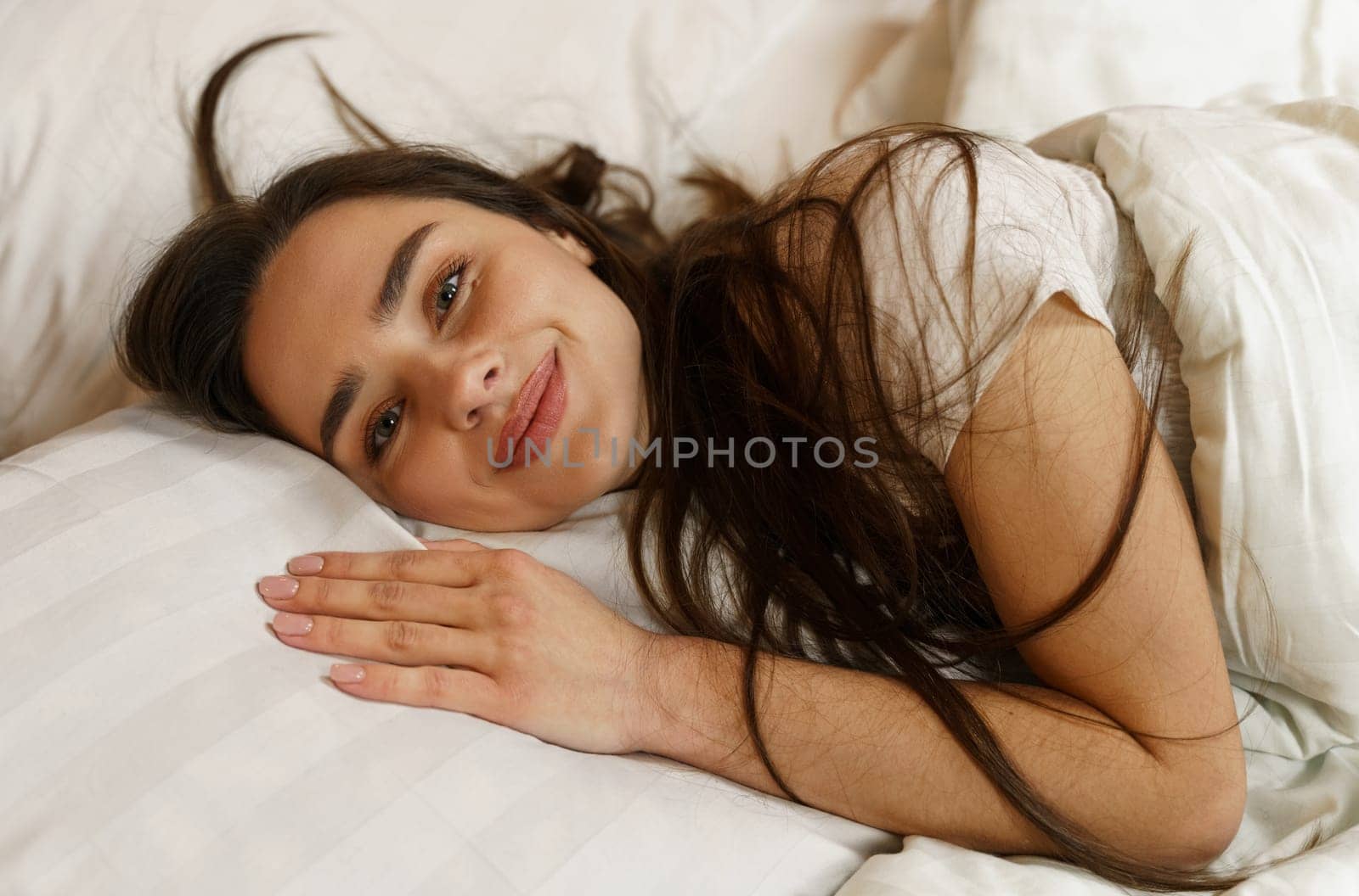 A young woman lying in bed woke up after a dream, flirting, smiling, looking at the camera.