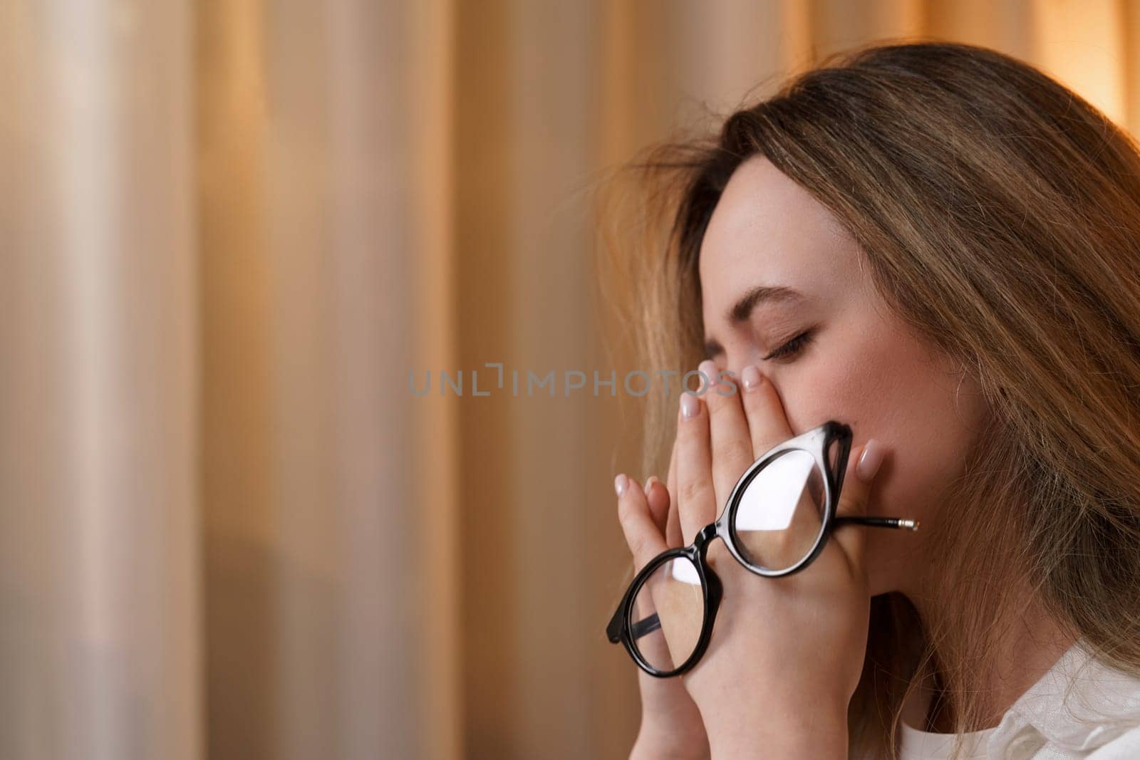 Young woman rubs her eyes, suffers from eye fatigue, holding glasses in her eyes. Concepts of eye diseases
