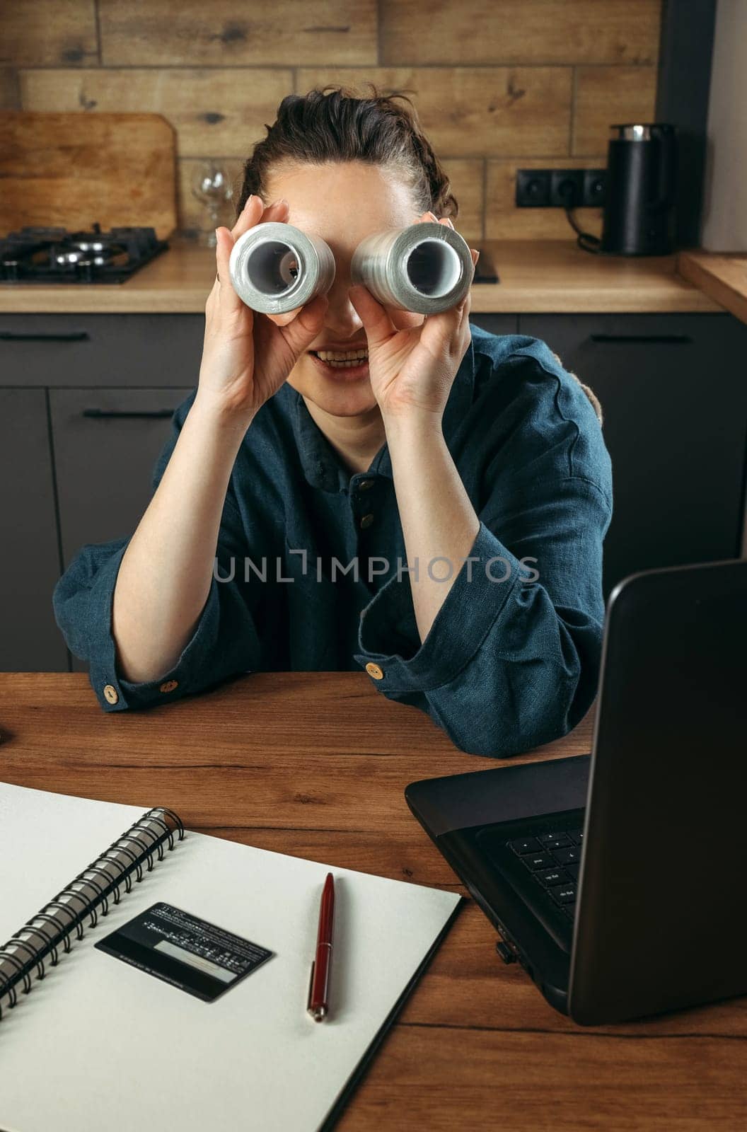 Portrait of a beautiful cheerful female clothing stylist who sits at a table near a laptop and looks through large spools of thread. Vertical frame.