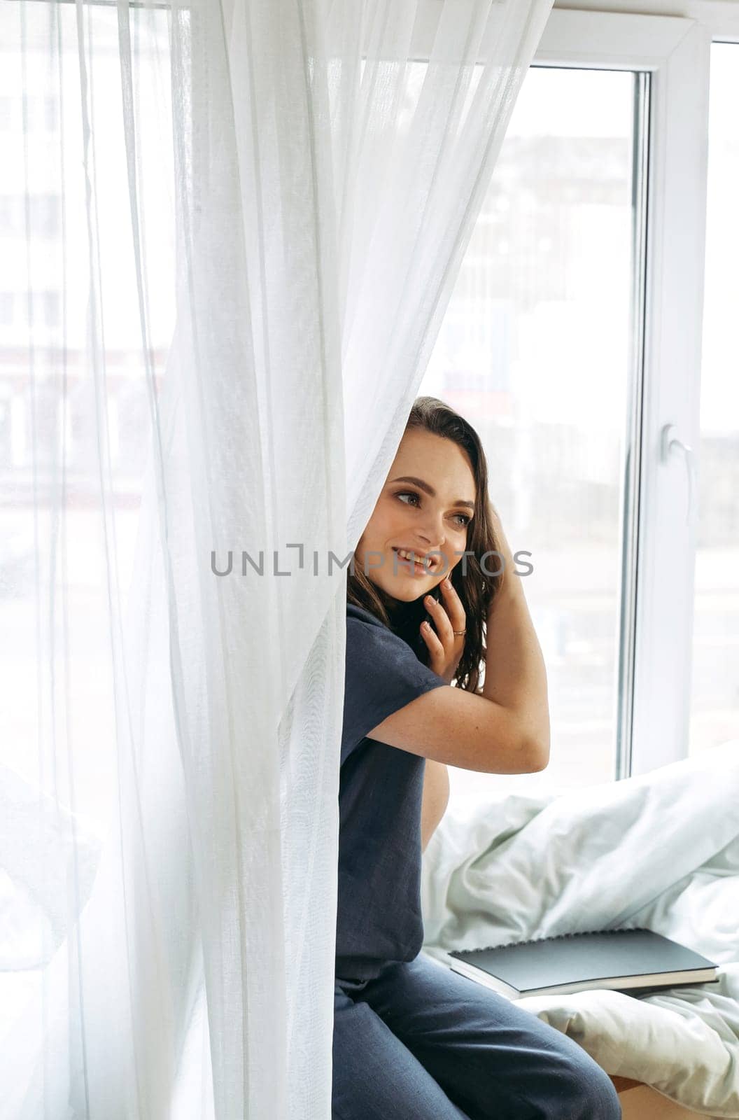 Young woman sitting on the windowsill talking on the phone. Vertical frame.