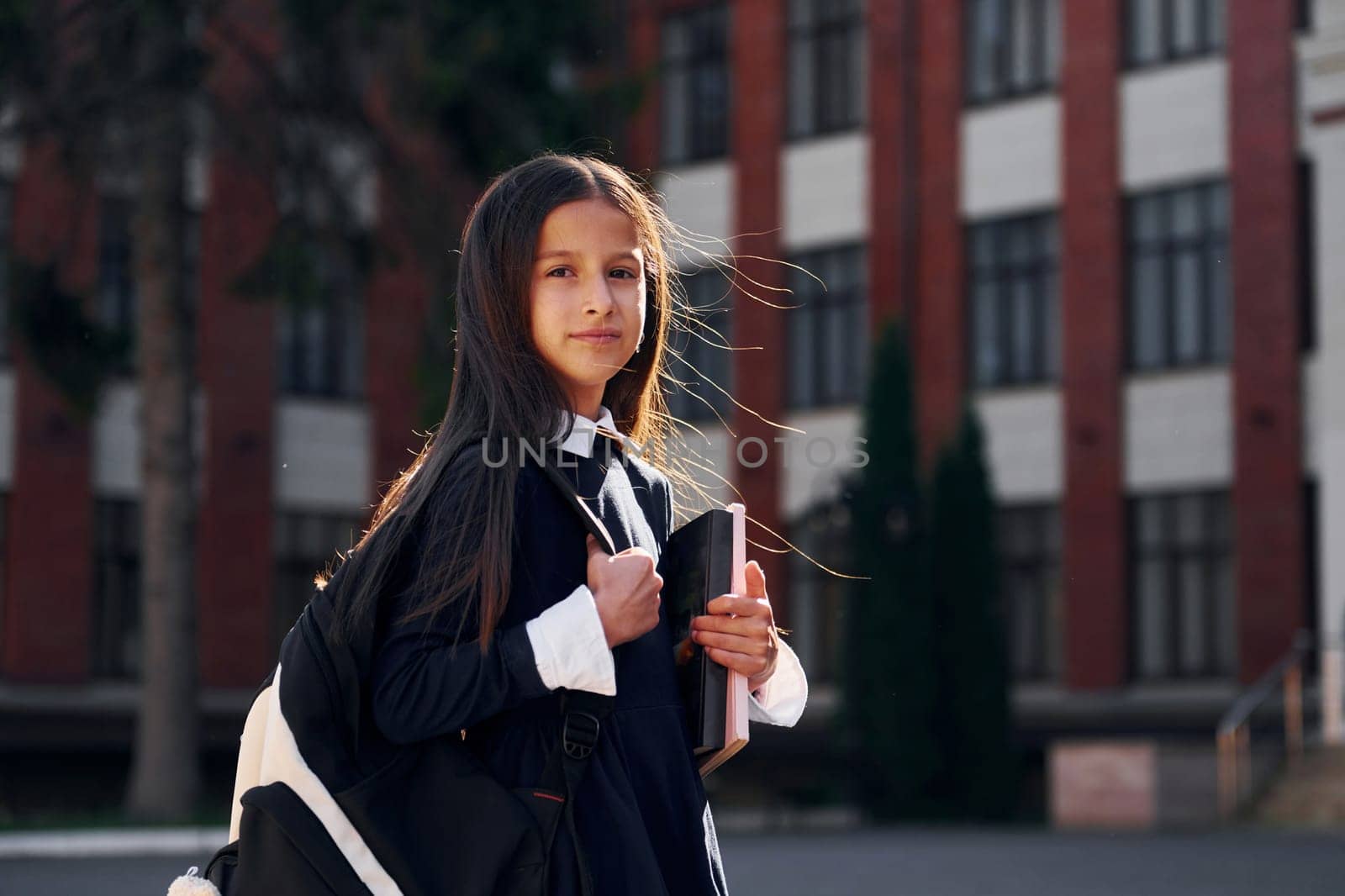 Having a walk. Schoolgirl is outside near school building.