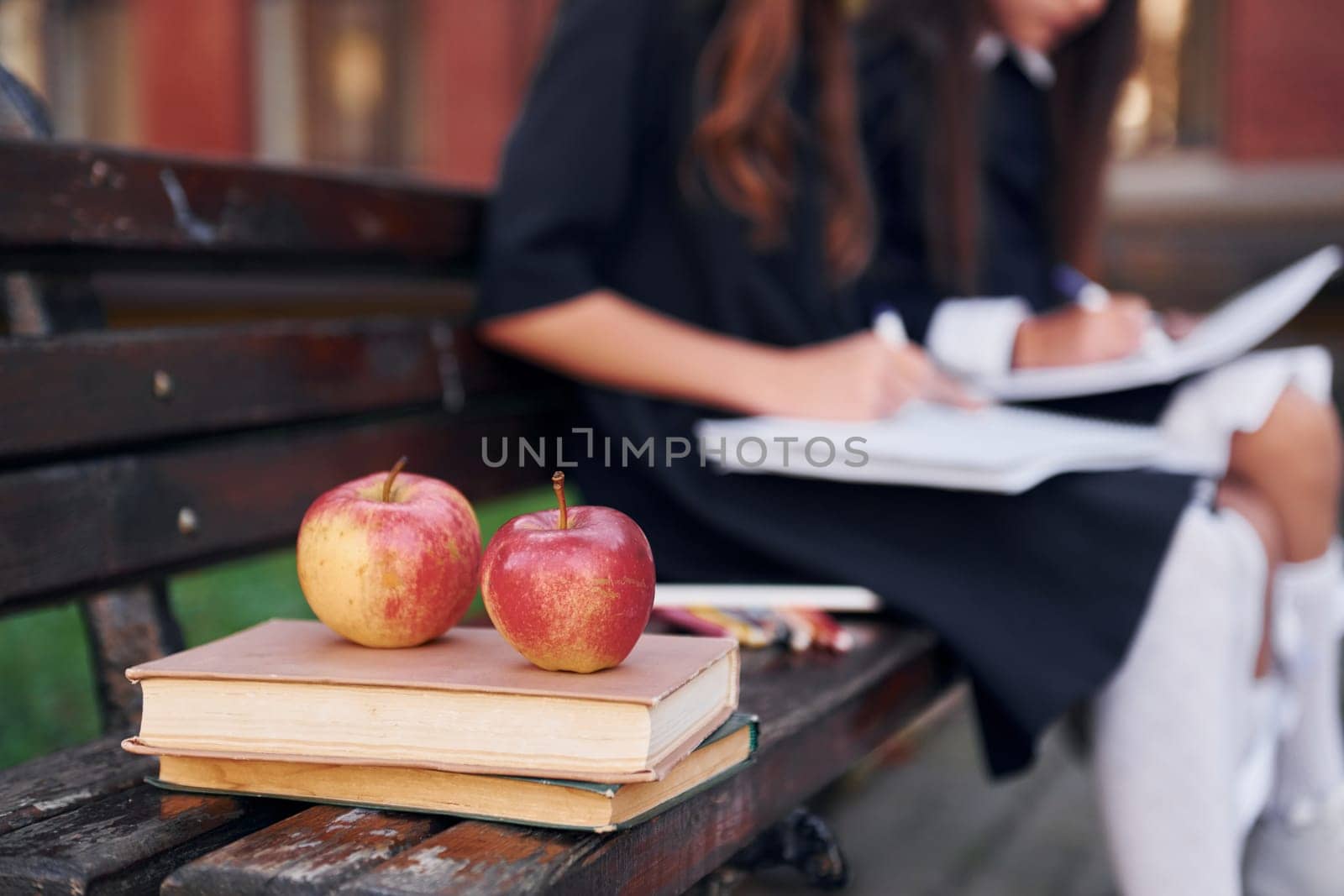 Apples is on the book. Two schoolgirls is outside together near school building.