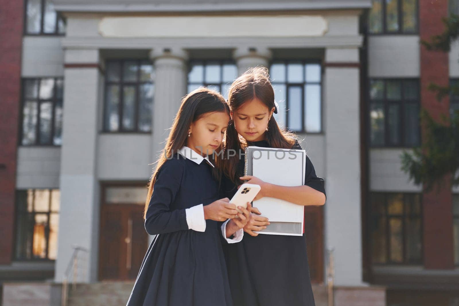 Front view. Two schoolgirls is outside together near school building.