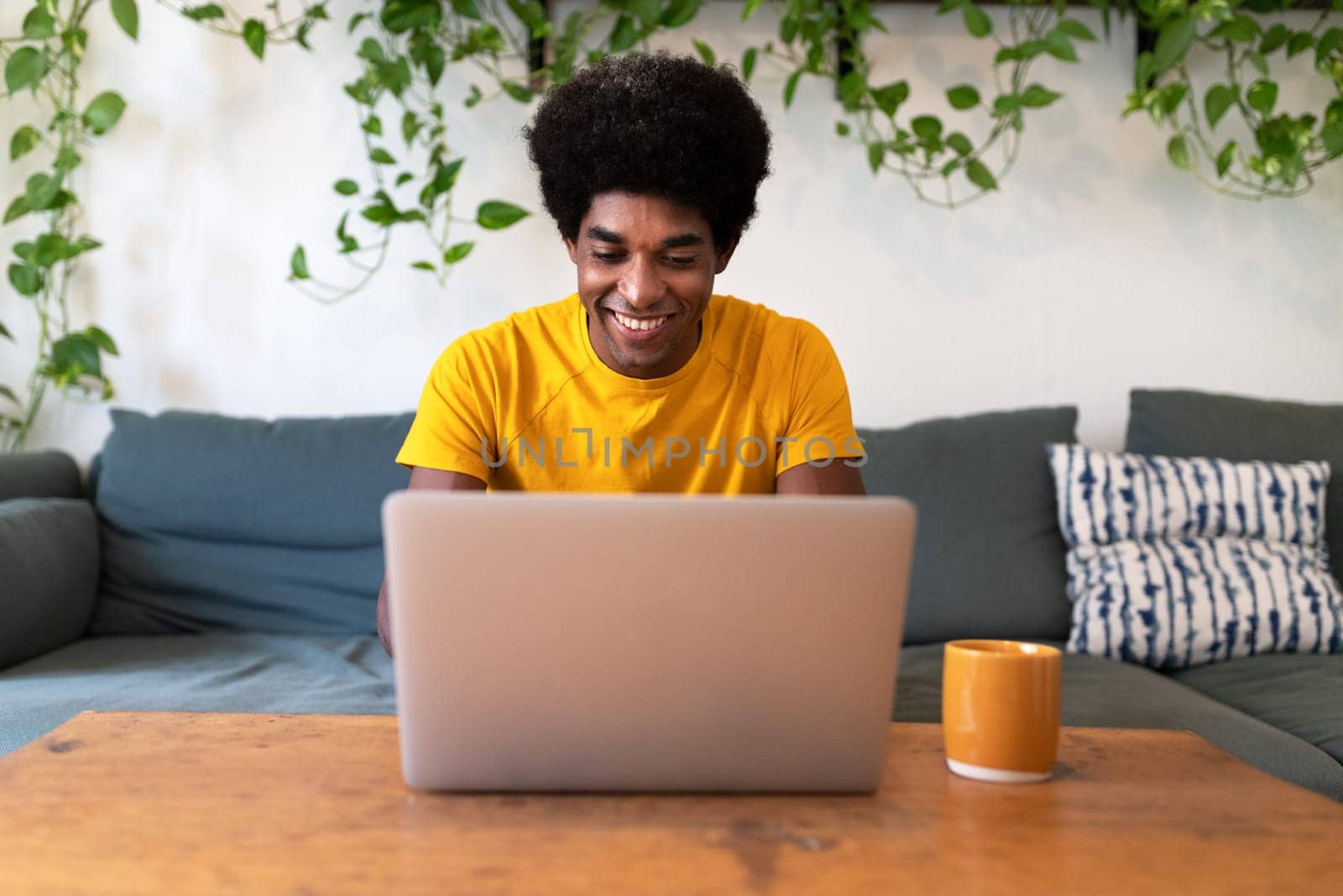 Smiling young african american man sitting on the sofa checking email with laptop. Technology concept. At home concept.