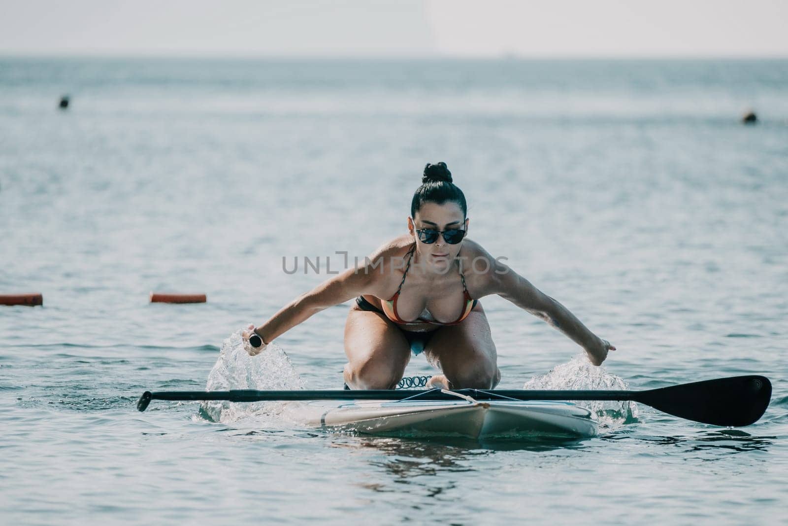 Sea woman sup. Silhouette of happy middle aged woman in rainbow bikini, surfing on SUP board, confident paddling through water surface. Idyllic sunset. Active lifestyle at sea or river